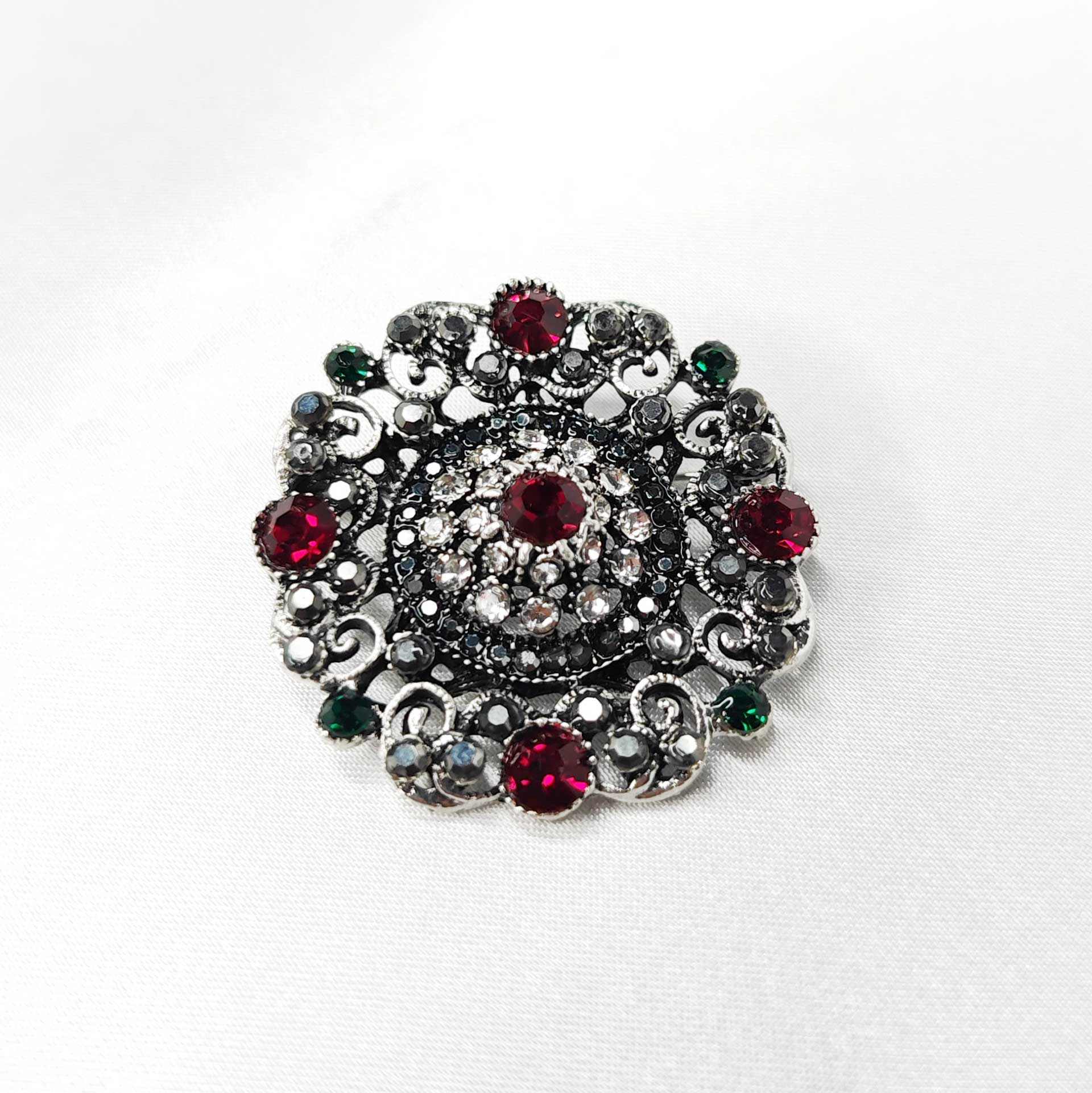 Photo 2 de la broche style baroque en forme de rosace mandala ornée de 5 strass rouges cardinaux et des éclats de strass verts, noir et blanc.