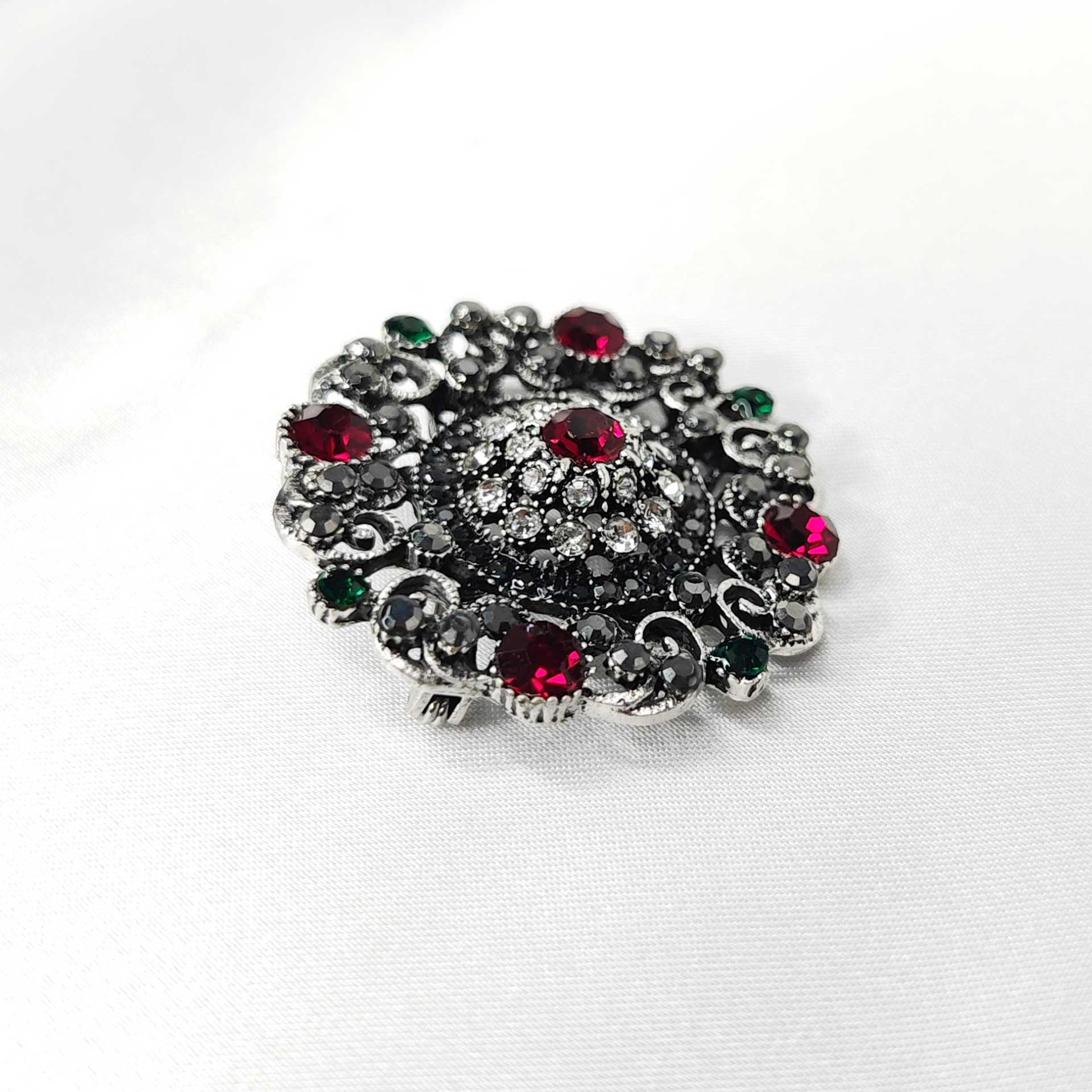 Photo 3 de la broche style baroque en forme de rosace mandala ornée de 5 strass rouges cardinaux et des éclats de strass verts, noir et blanc.