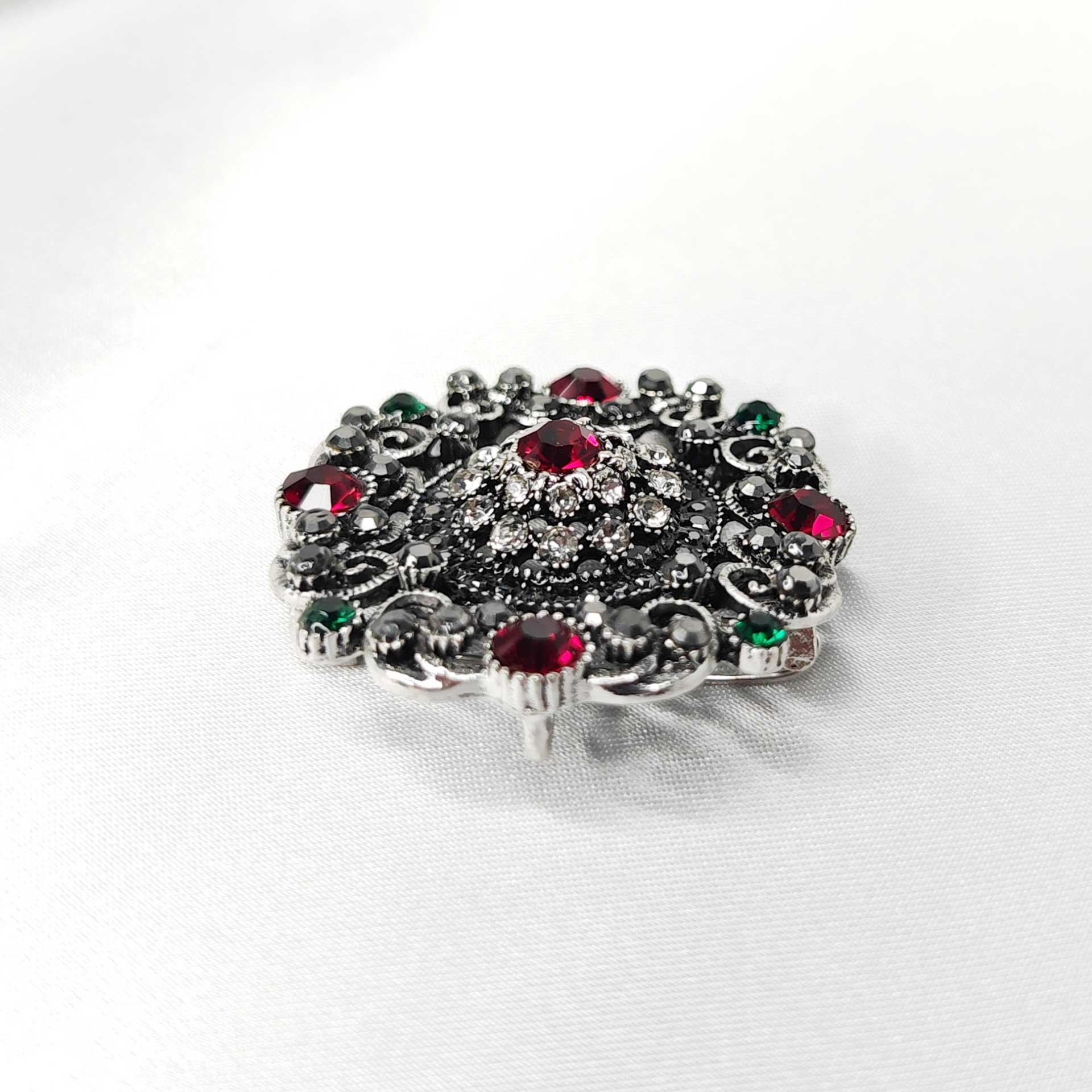 Photo 4 de la broche style baroque en forme de rosace mandala ornée de 5 strass rouges cardinaux et des éclats de strass verts, noir et blanc.