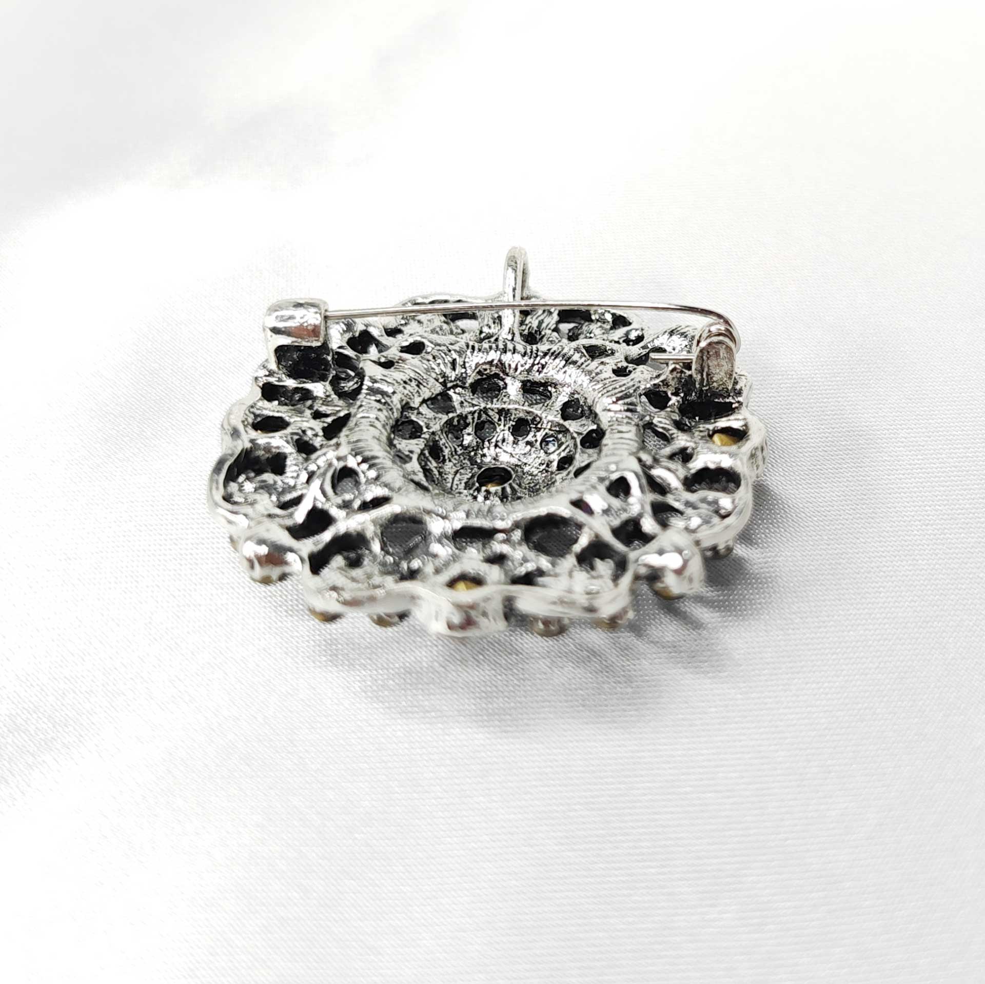 Photo du verso de la broche style baroque en forme de rosace mandala ornée de 5 strass rouges cardinaux et des éclats de strass verts, noir et blanc.