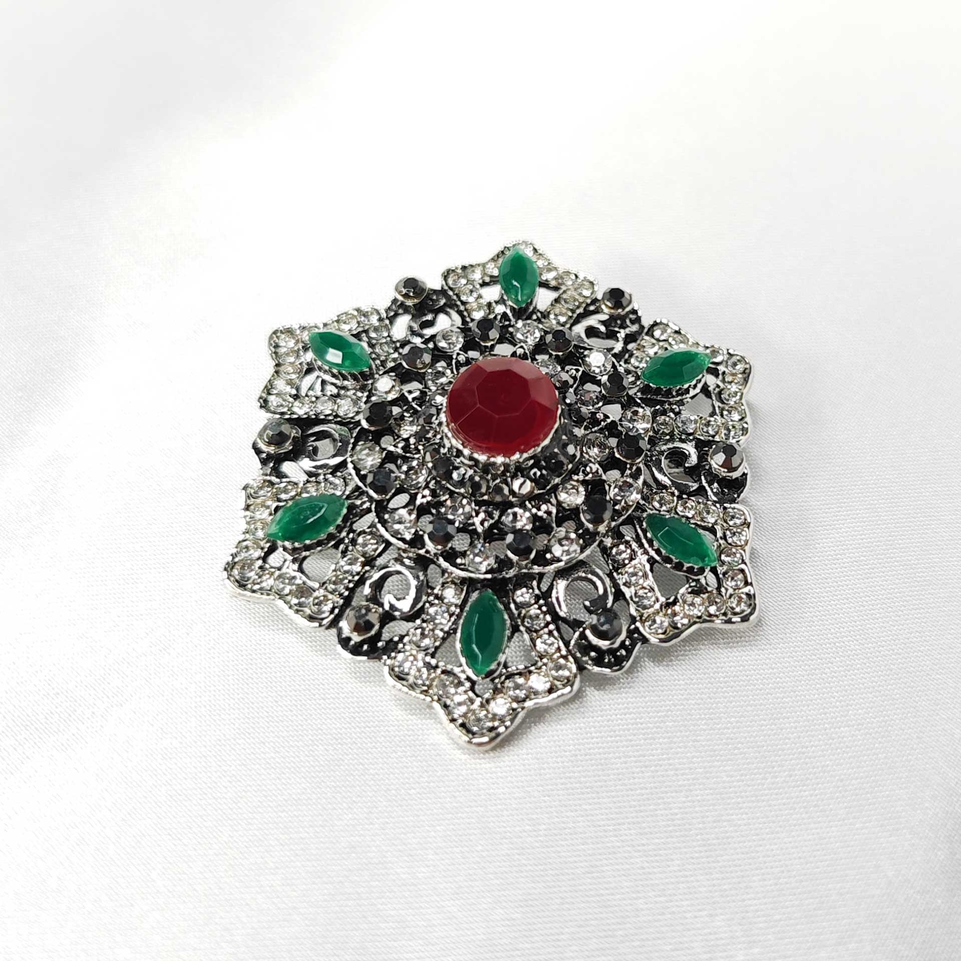 Photo 2 de la broche style baroque a la forme étoilée florale ornée d'un strass rouge centrale.