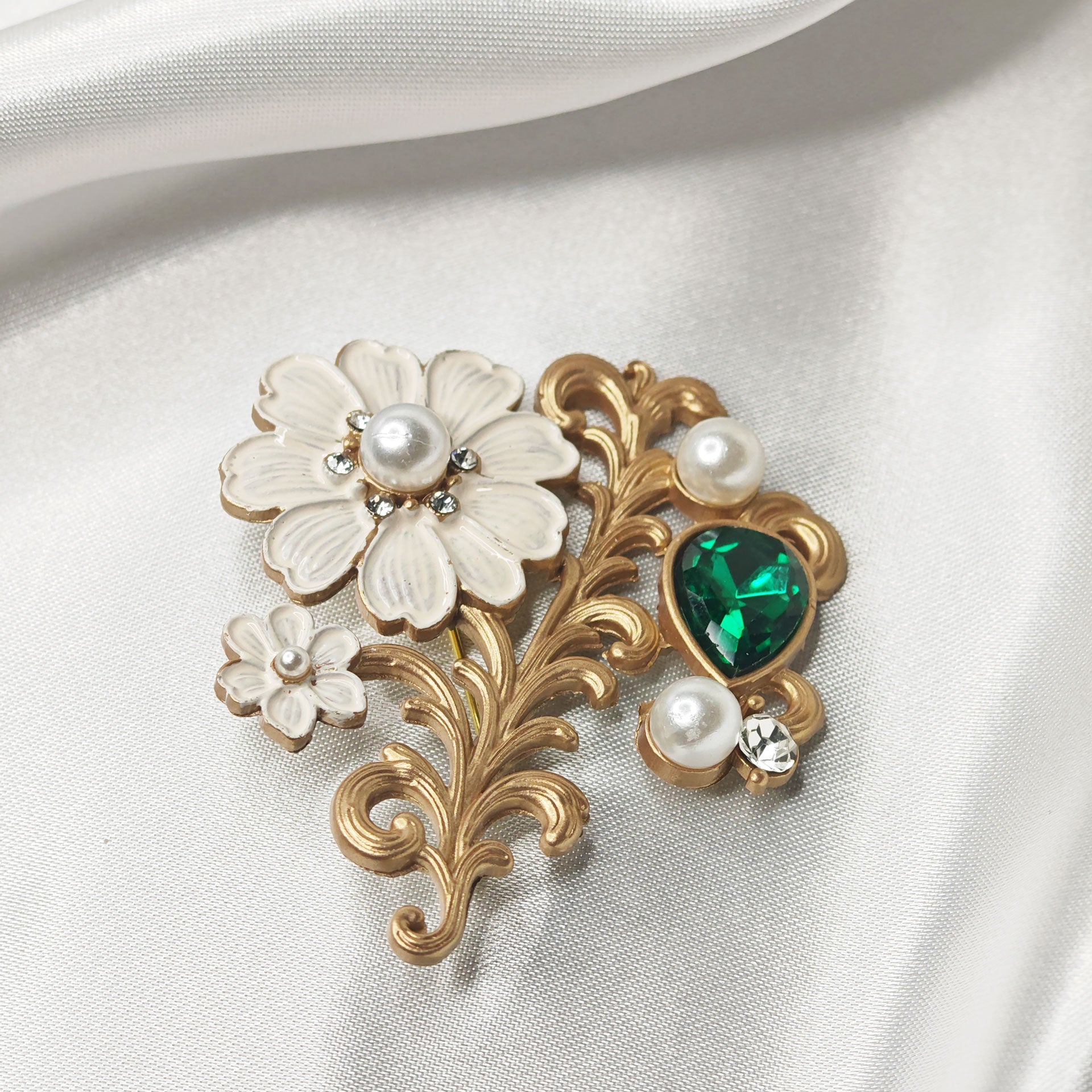 Broche fleur blanche style baroque avec arabesques dorées, perles et cristal vert en goutte sur tissu satiné