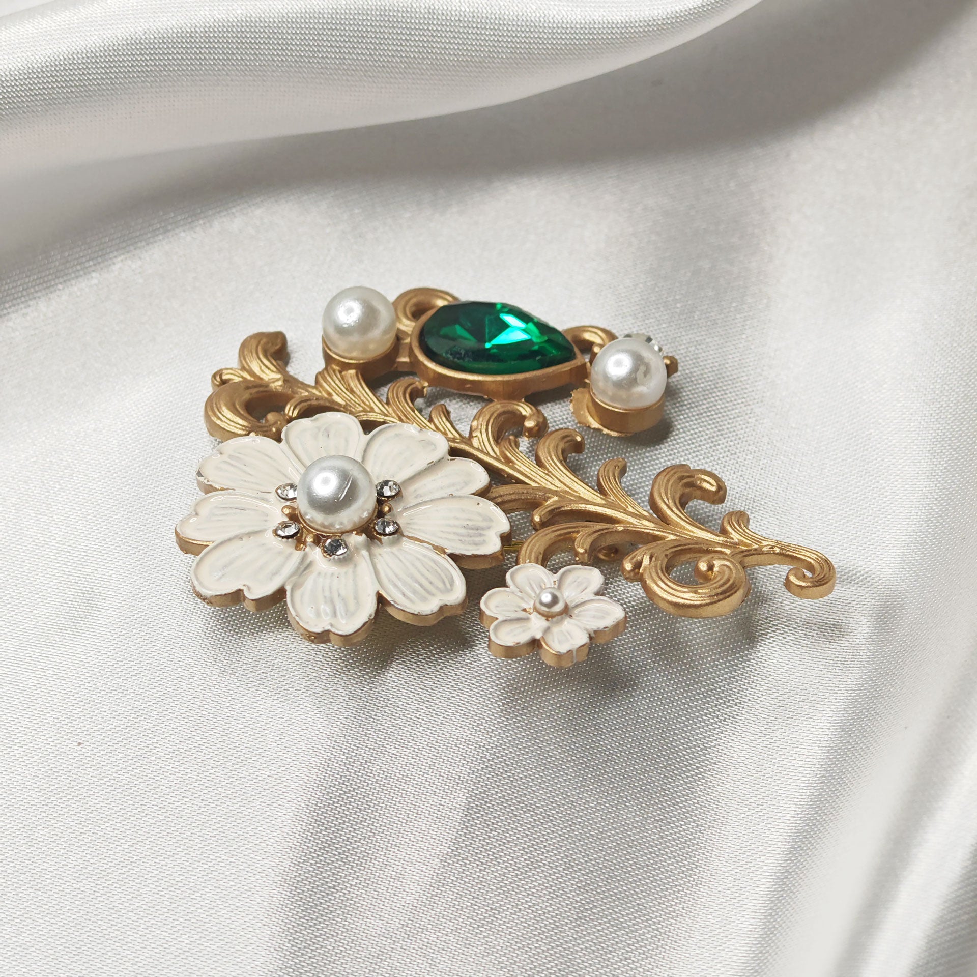 Détail broche bijou fleur de cerisier blanche avec perle centrale et strass, ornée d’un cristal vert émeraude