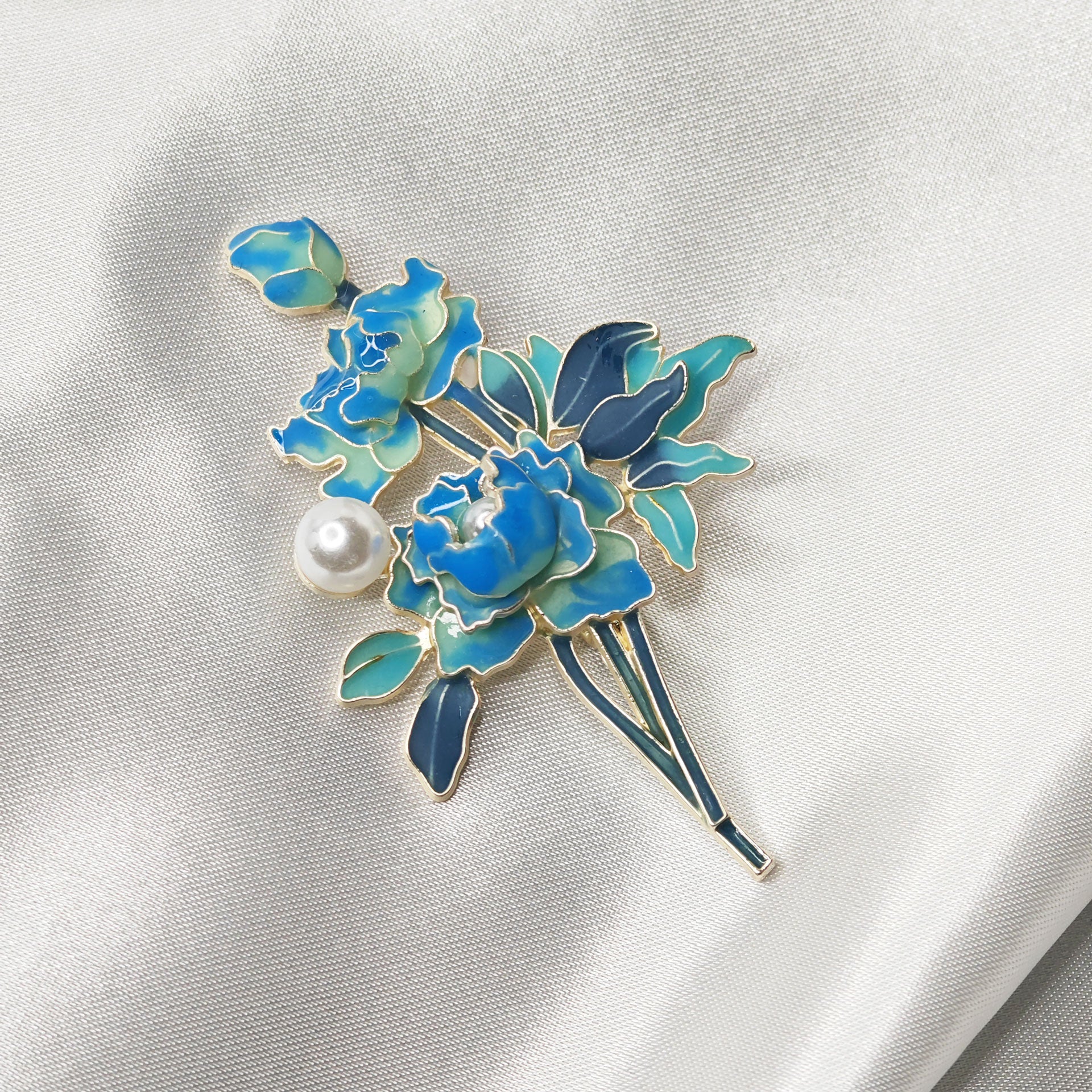 Broche pivoine bleue émaillée avec perle et finitions dorées sur tissu satiné