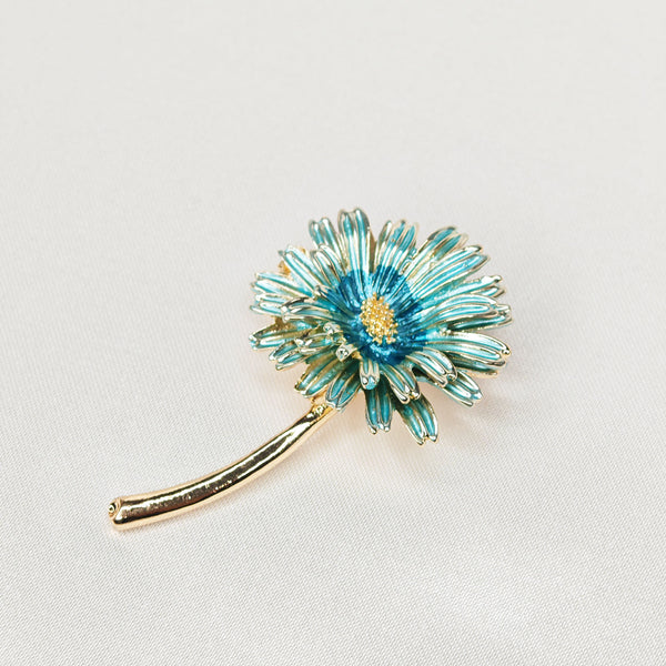 Broche dorée en forme de marguerite de couleur bleue.