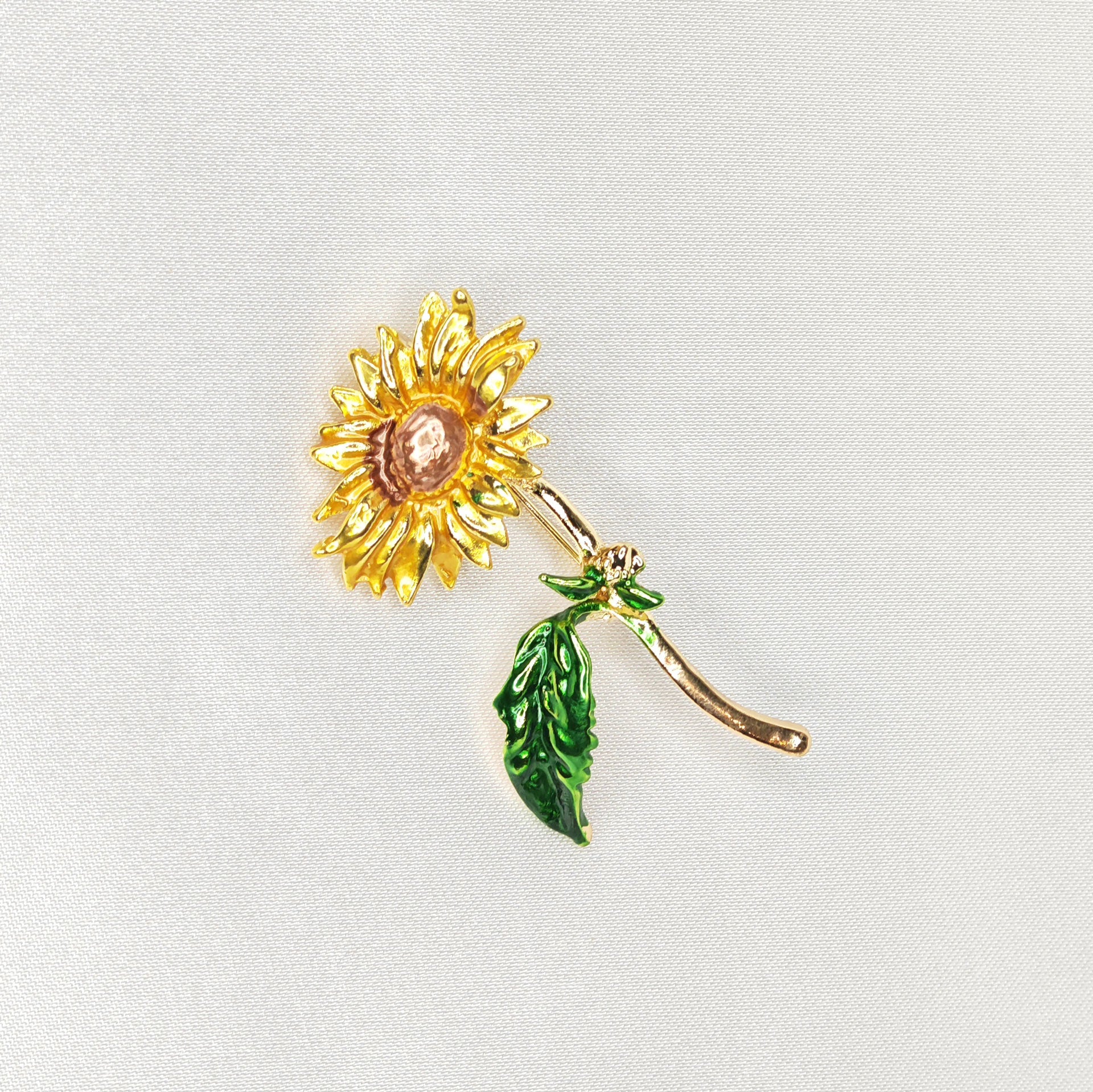 Broche dorée en forme de fleur de tournesol jaune et tige verte.