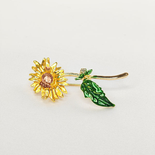 Broche dorée en forme de fleur de tournesol jaune et tige verte.