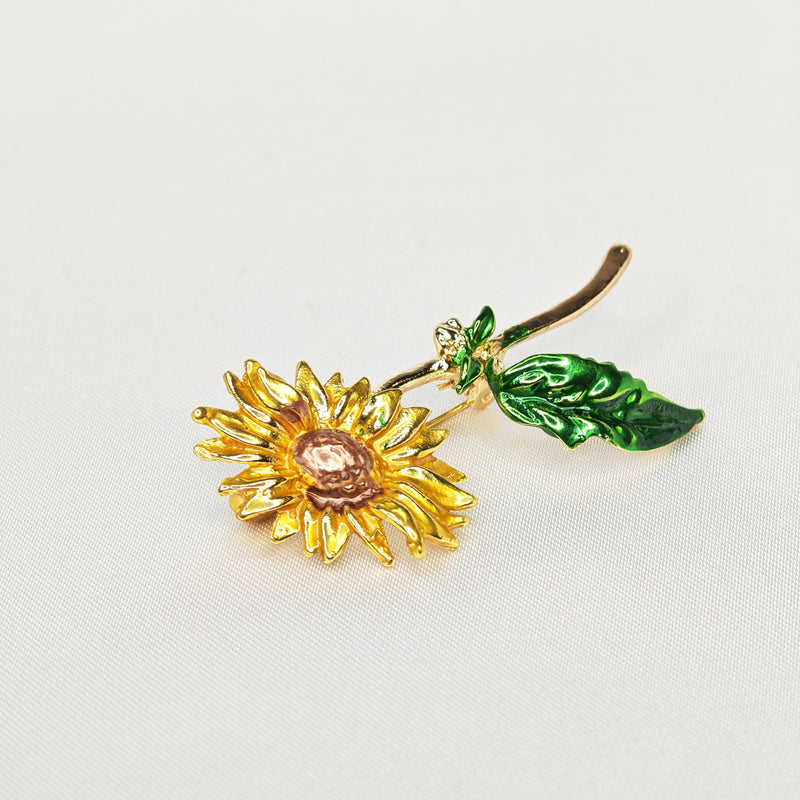 Broche dorée en forme de fleur de tournesol jaune et tige verte.