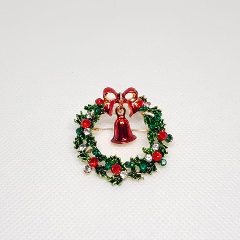 Broche dorée en forme de couronne de noel avec un cloche rouge en son centre et des strass effet diamant.