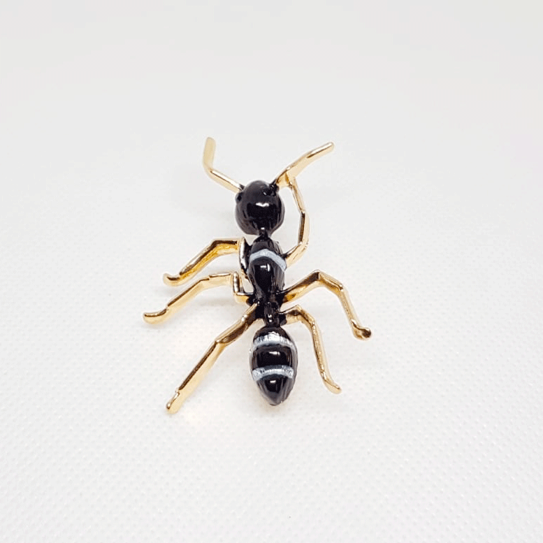 Broche dorée en forme de fourmi noir et rayures blanches.