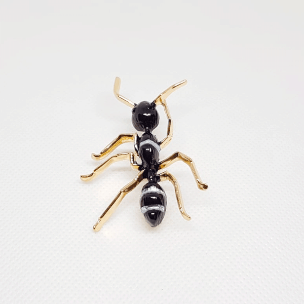 Broche dorée en forme de fourmi noir et rayures blanches.