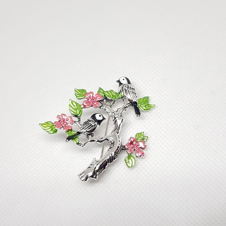 Broche argentée en forme de branche d'arbre fleuri et oiseaux perchés.