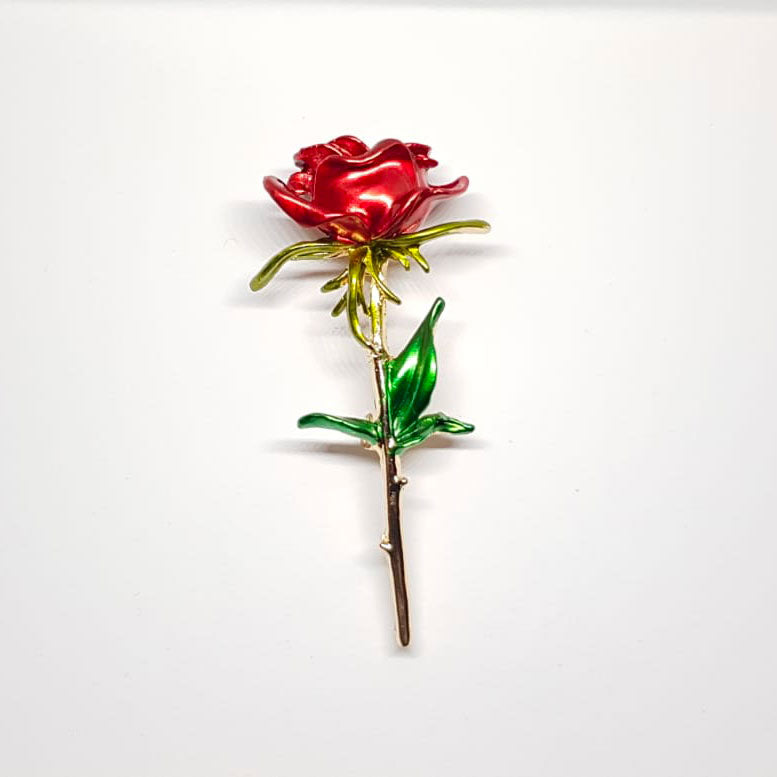 Broche dorée en forme de rose rouge et pétales vertes.