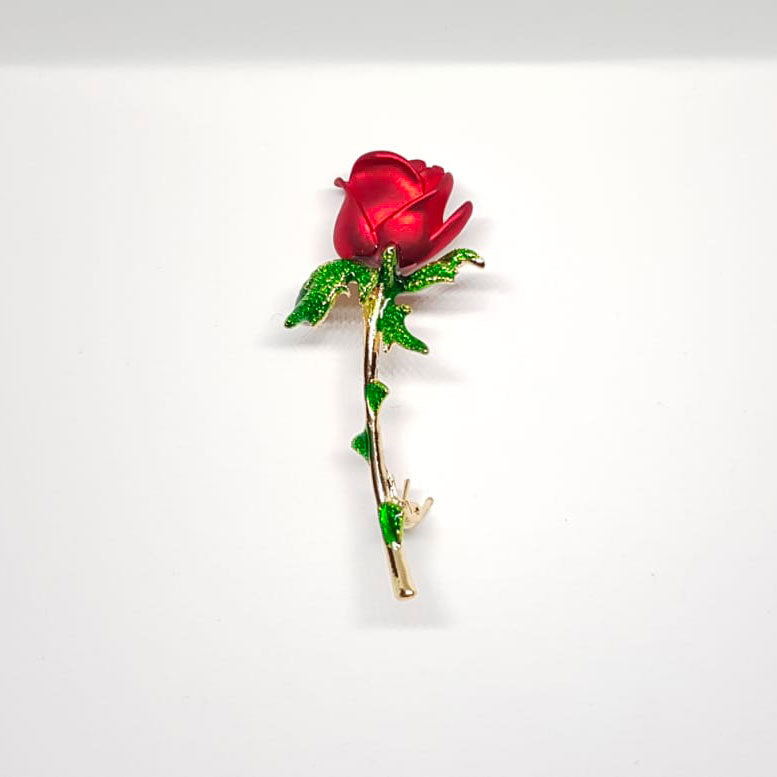 Broche dorée en forme de rose rouge, pétale et épine verte.