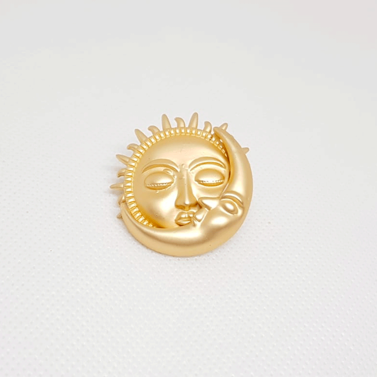 Broche dorée en forme de visage de soleil et lune s'embrassant.