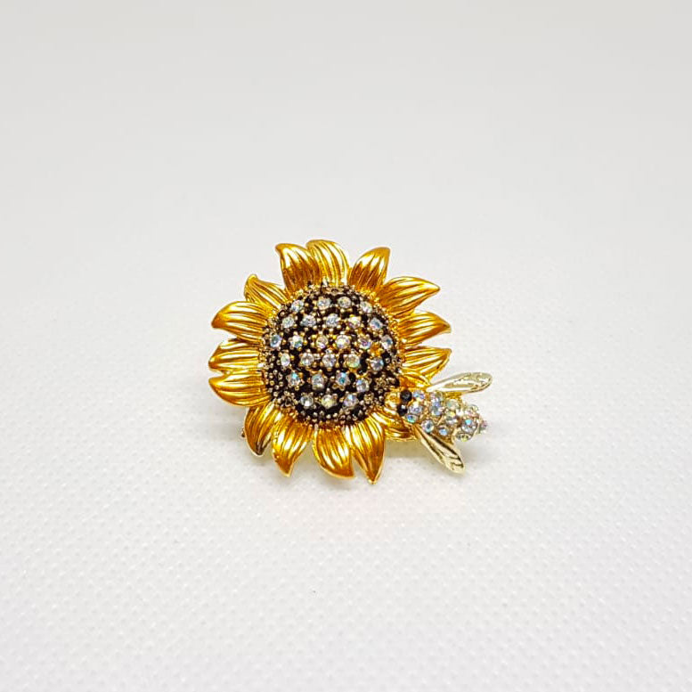 Broche dorée en forme de fleur de tournesol avec une abeille posée dessus.